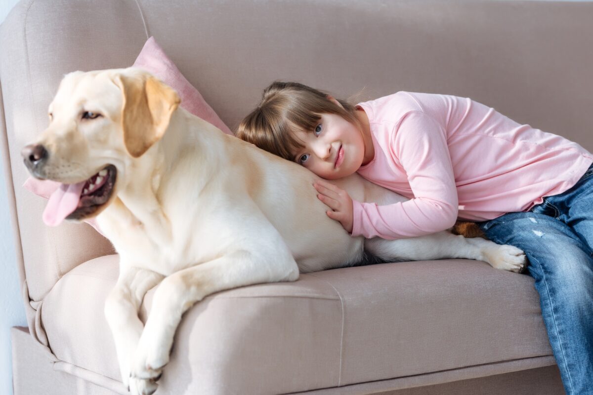 Enfant atteint du syndrome de Down allongé sur le canapé avec son chien Labrador retriever