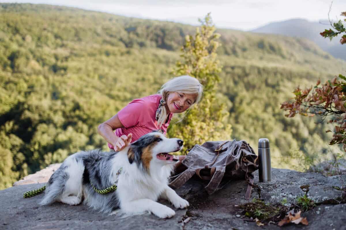 Senior woman resting and stroking her dog during walking in forest.
