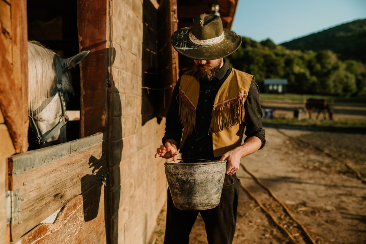 Portrait of horse breeder with bucket of food taking care of animal.